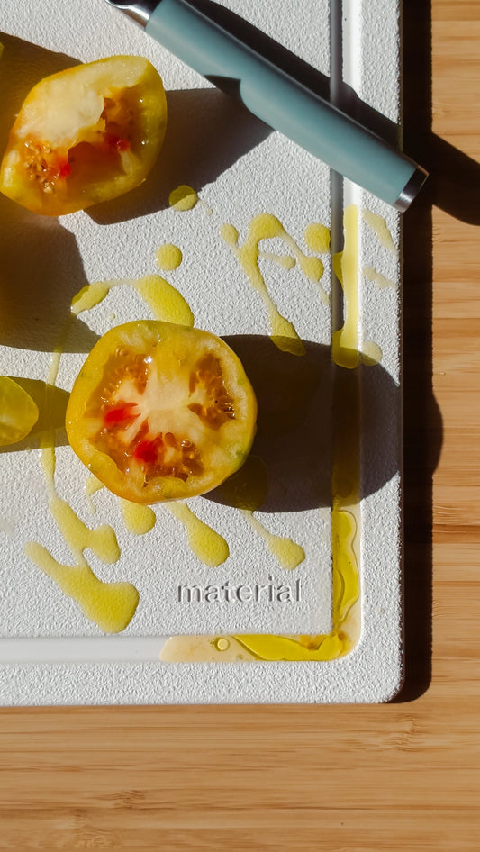 Tomato halves on a cutting board with a knife, branded 'material'.