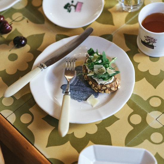 Table setting with a plate of food, cutlery, and a cup on a patterned tablecloth.