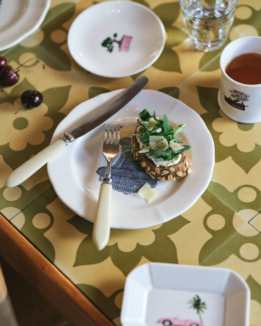 Table setting with a plate of food, cutlery, and a cup on a patterned tablecloth.