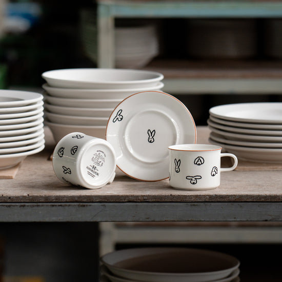 Set of white ceramic plates and mugs with decorative designs on a wooden table.