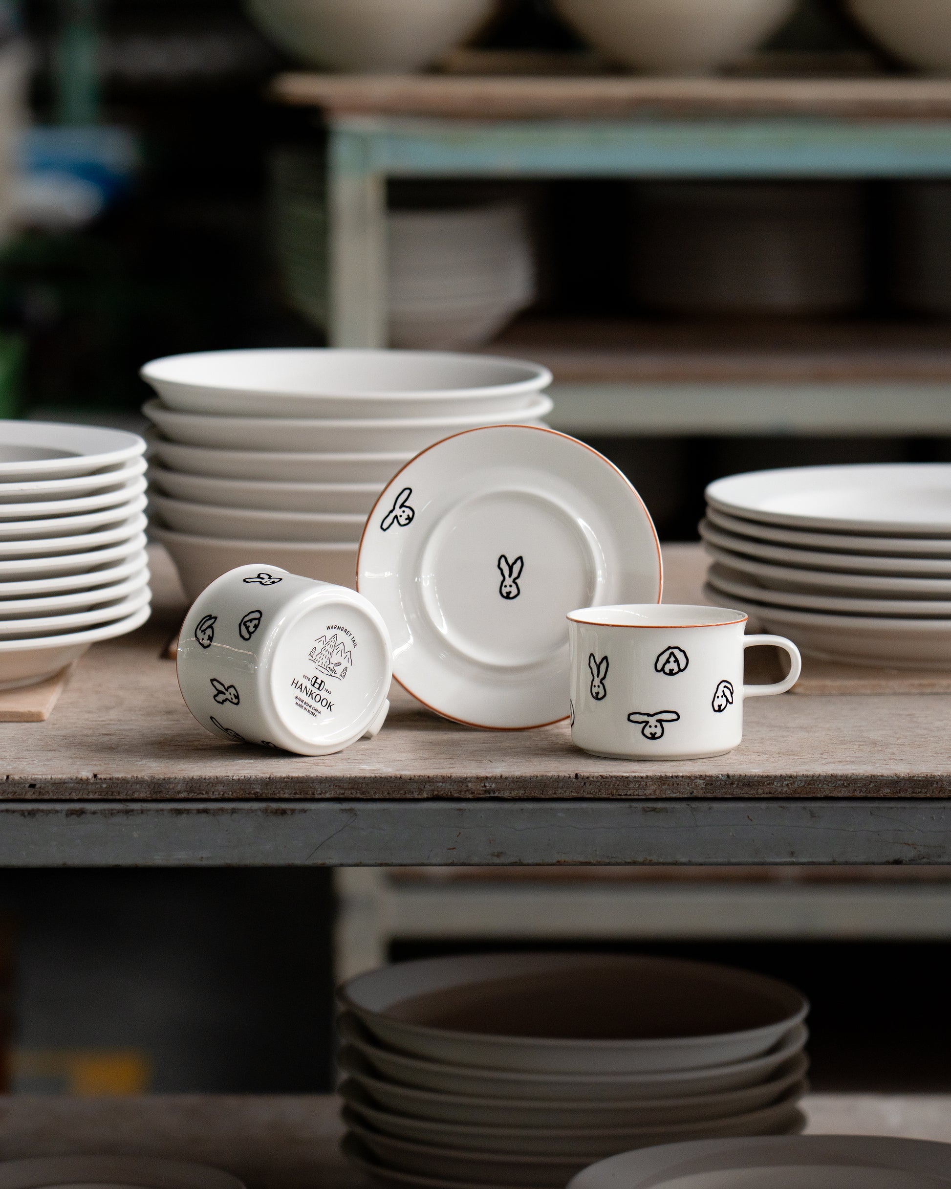 Set of white ceramic plates and mugs with decorative designs on a wooden table.