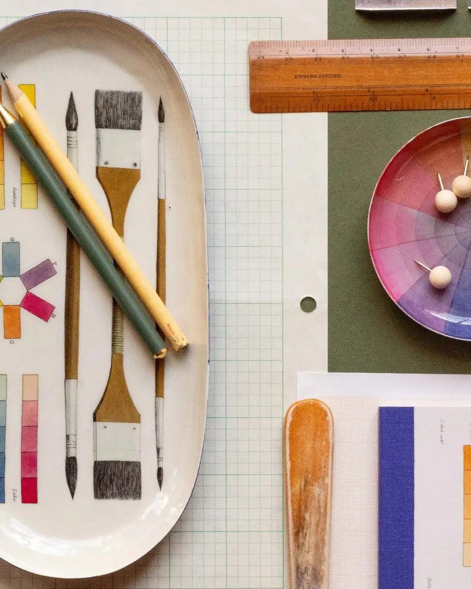 Art supplies including brushes, a color wheel, and a ruler on a green surface.