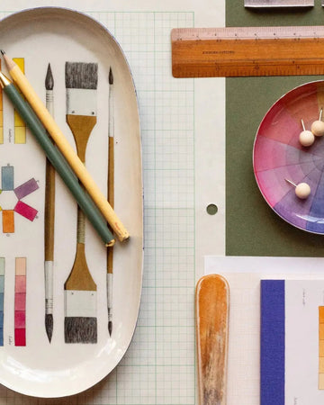 Art supplies including brushes, a color wheel, and a ruler on a green surface.