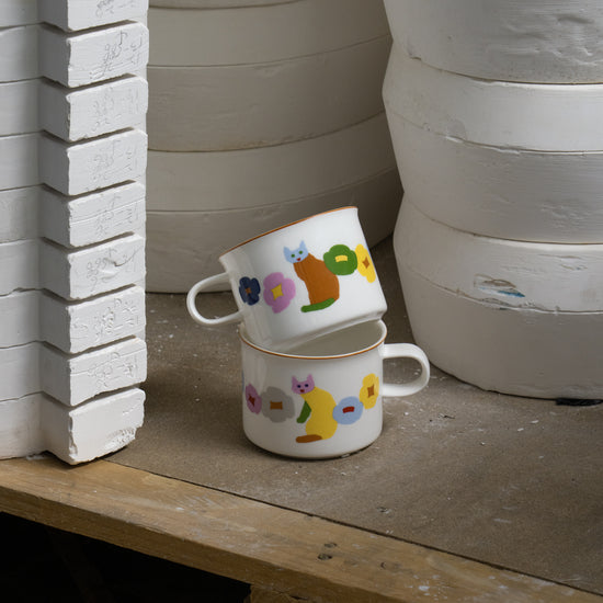 Two ceramic cups with animal illustrations on a wooden surface next to stacked clay pots.