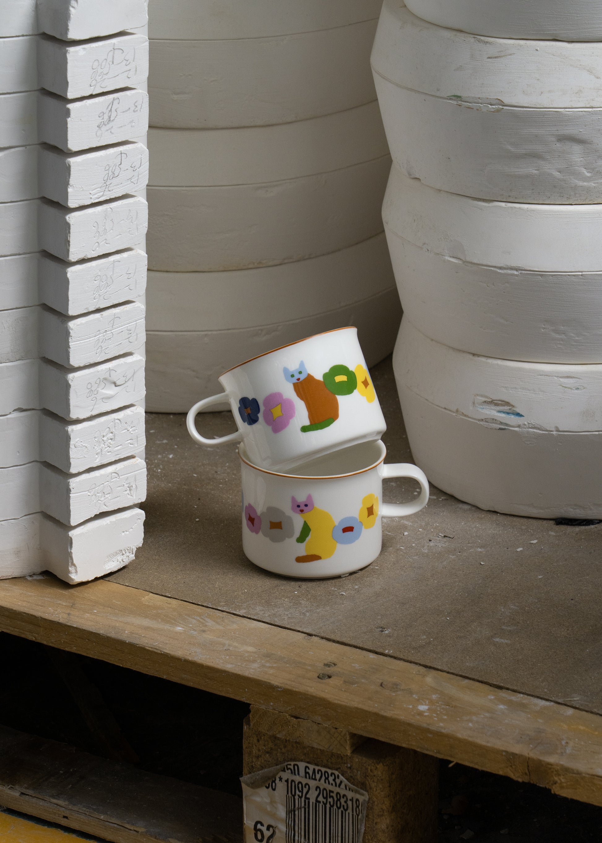 Two ceramic cups with animal illustrations on a wooden surface next to stacked clay pots.