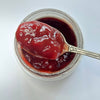 A spoon scooping glossy red fruit jam from an open jar