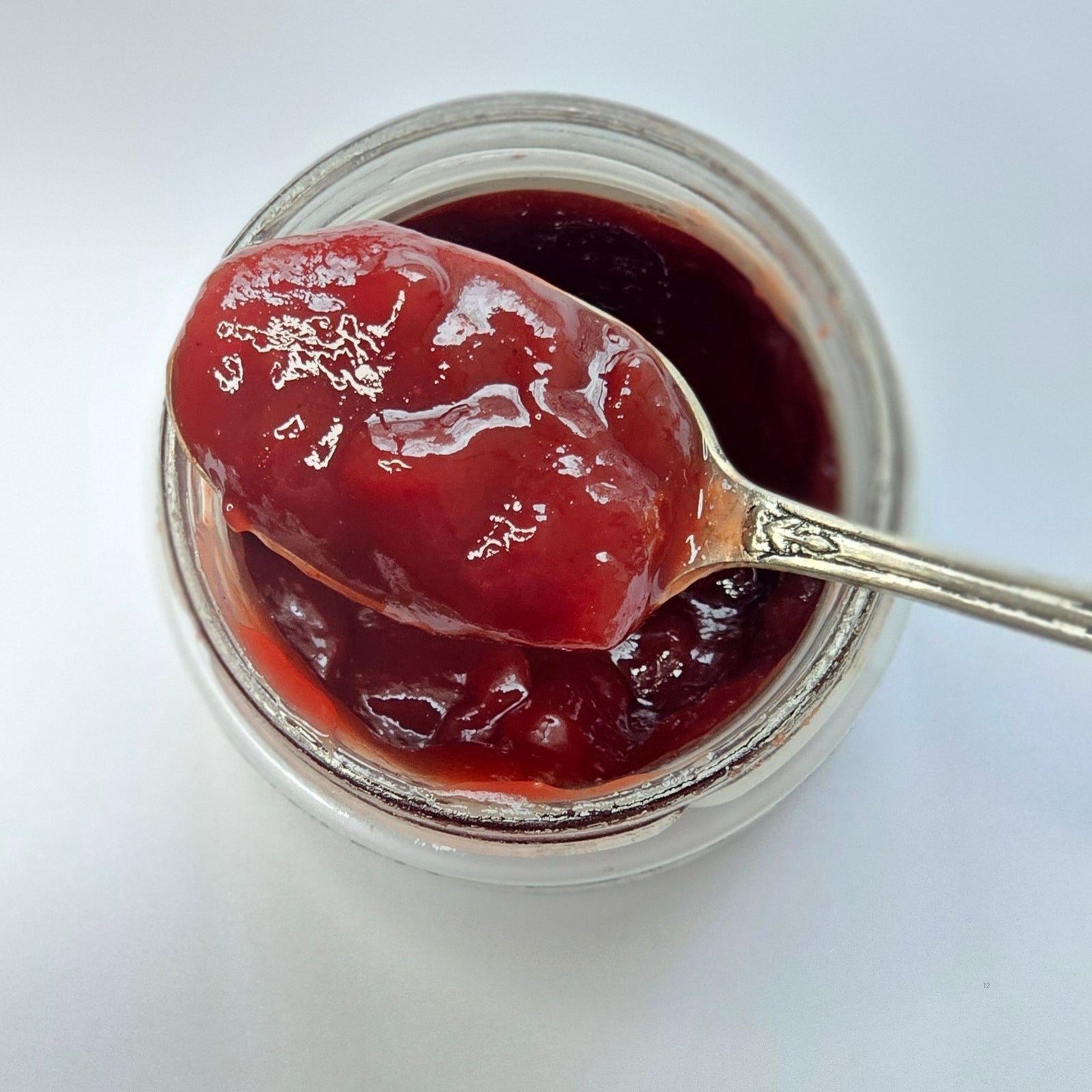 A spoon scooping glossy red fruit jam from an open jar