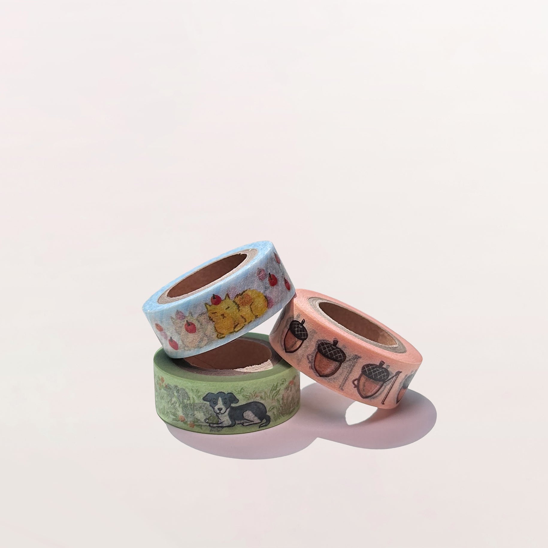 Three rolls of decorative tape with animal and acorn illustrations on a light pink background