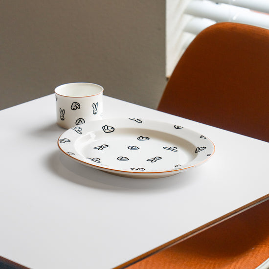 White ceramic plate with black patterns on a white table with orange chairs.