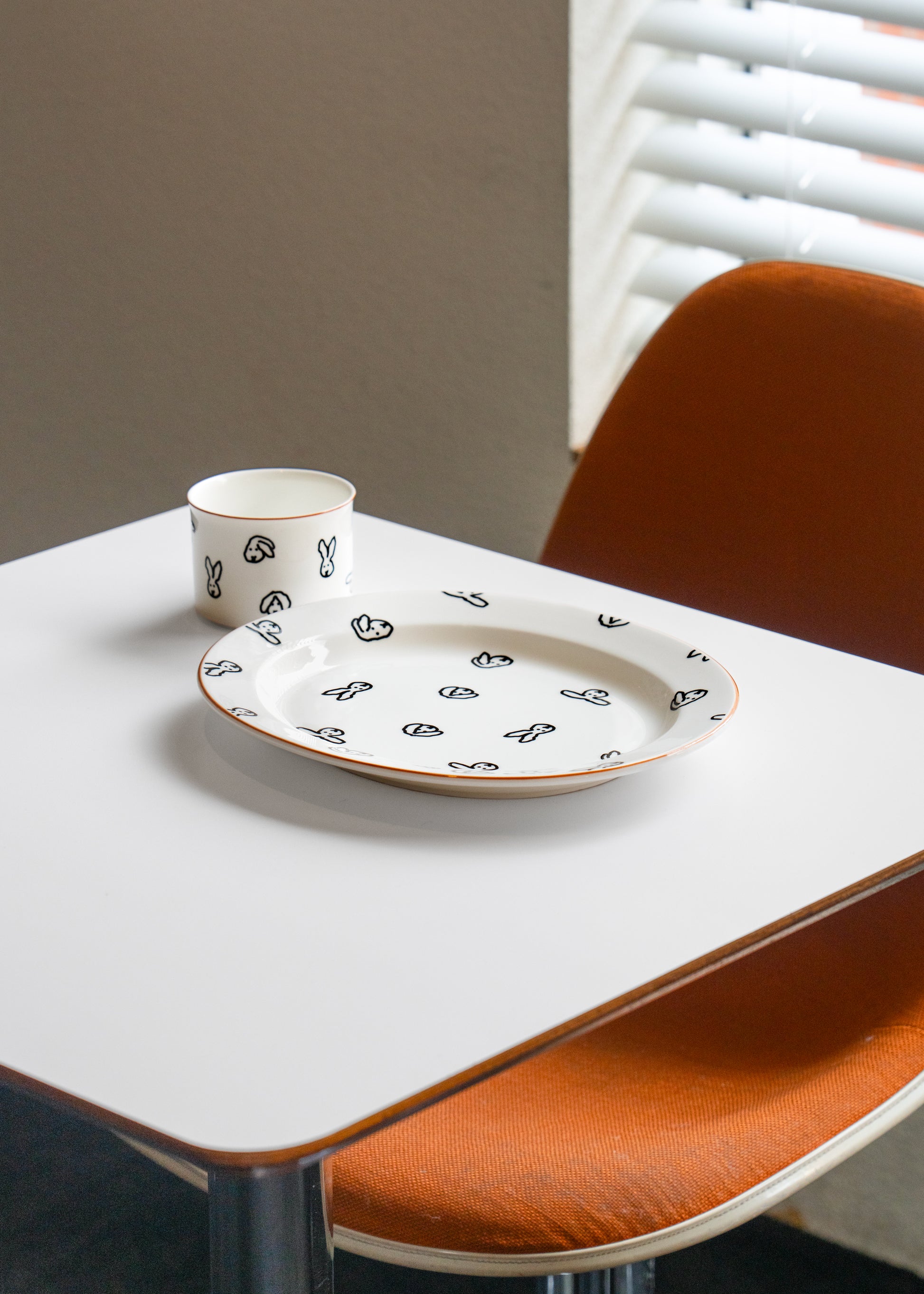 White ceramic plate with black patterns on a white table with orange chairs.