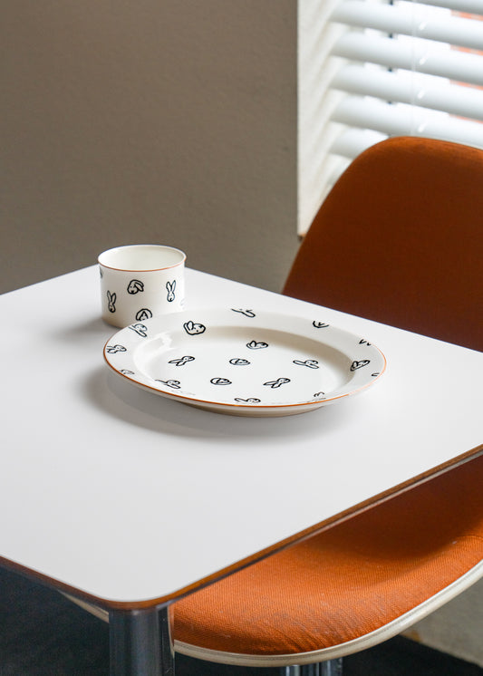 White ceramic plate with black patterns on a white table with orange chairs.