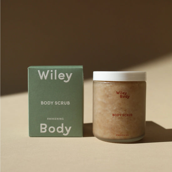 Wiley Body Scrub jar next to its green packaging box on a warm beige surface with soft shadows.