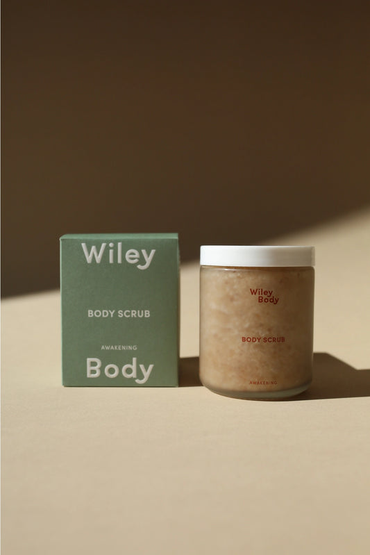 Wiley Body Scrub jar next to its green packaging box on a warm beige surface with soft shadows.