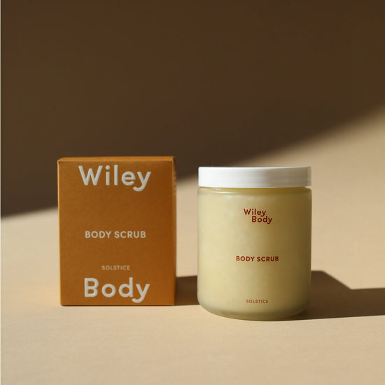 A jar of Wiley Body Scrub next to its brown cardboard packaging box on a warm beige surface with soft shadows.