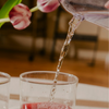 Tea being poured from a water carafe into a glass cup with a blurred background