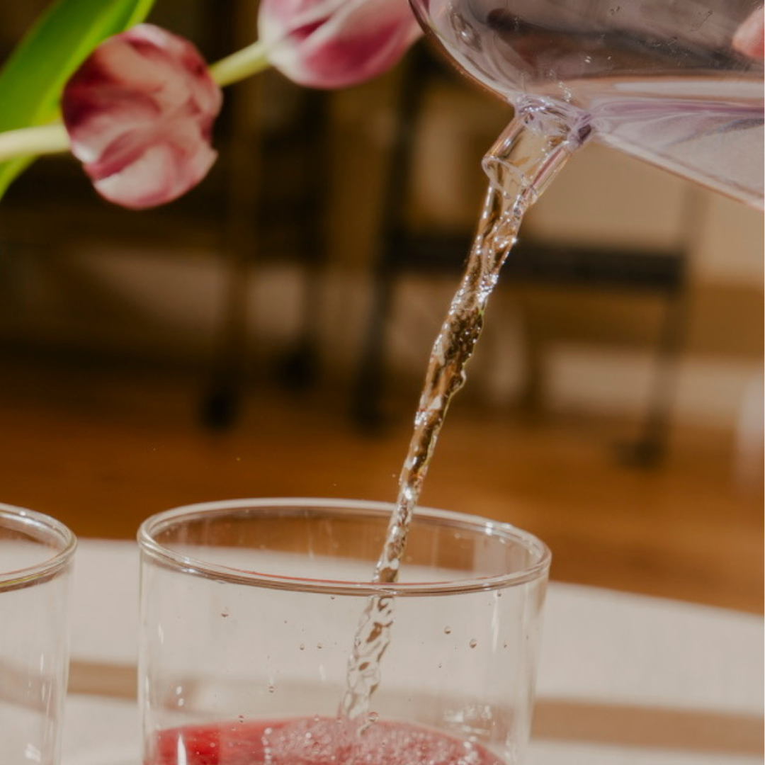 Tea being poured from a water carafe into a glass cup with a blurred background