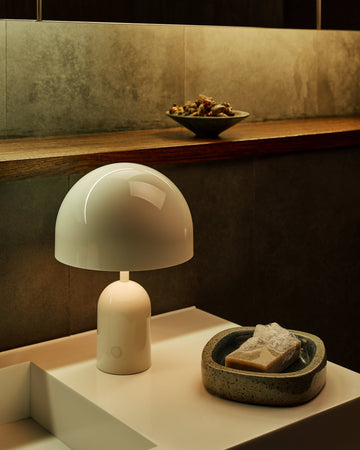 White lamp on a surface with a bowl of fruit in the background