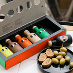 Colorful olive oil gift set in an open box, next to a plate of bread and olives.