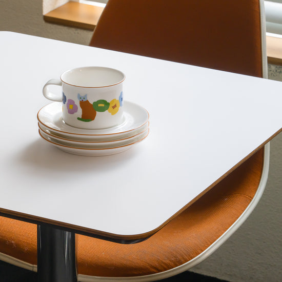 Teacup with colorful design on a stack of saucers on a white table.