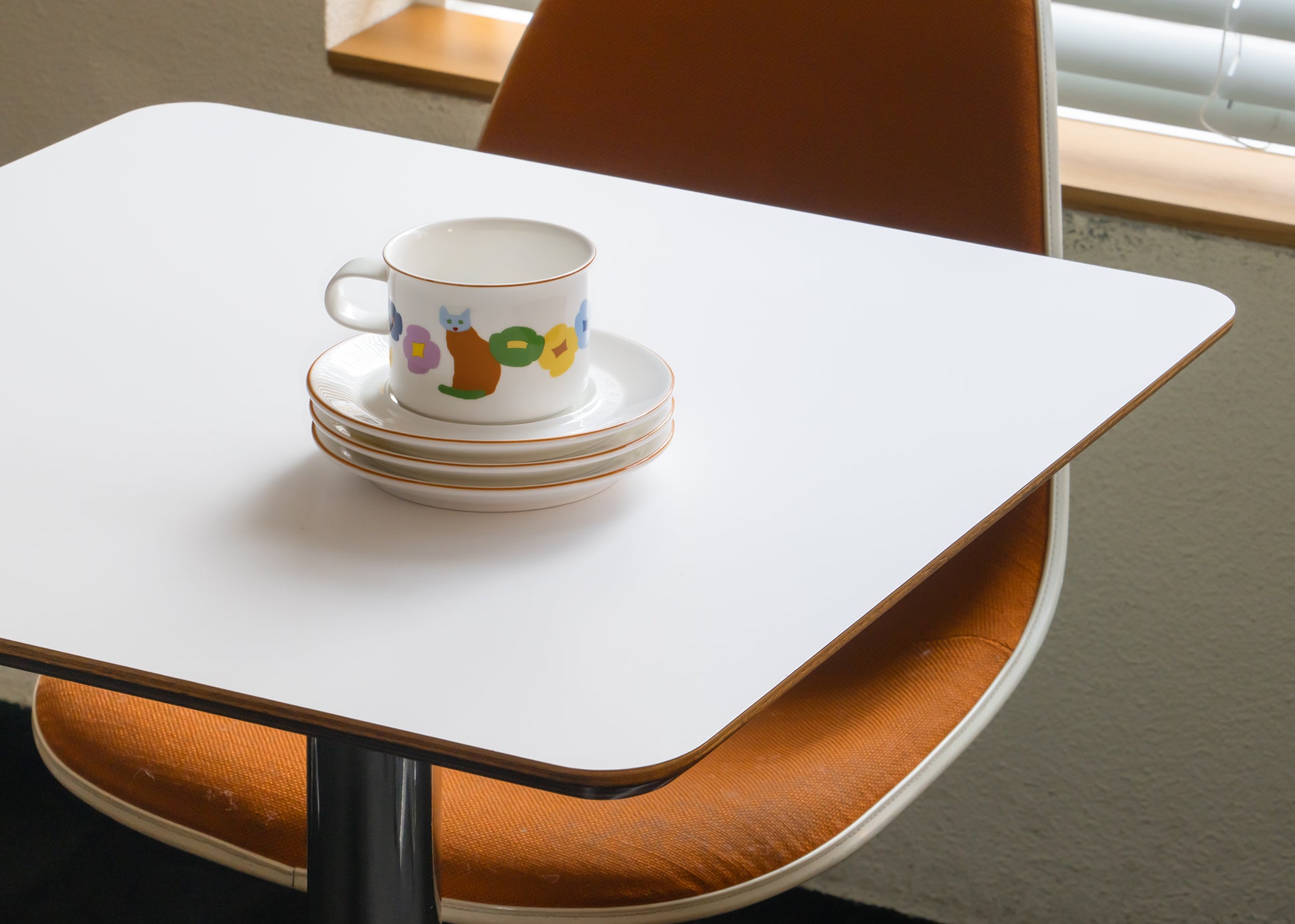 Teacup with colorful design on a stack of saucers on a white table.