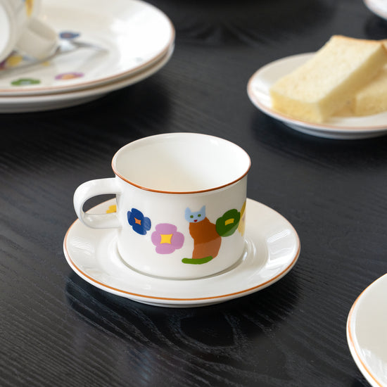Ceramic cup and saucer with colorful designs on a black table.