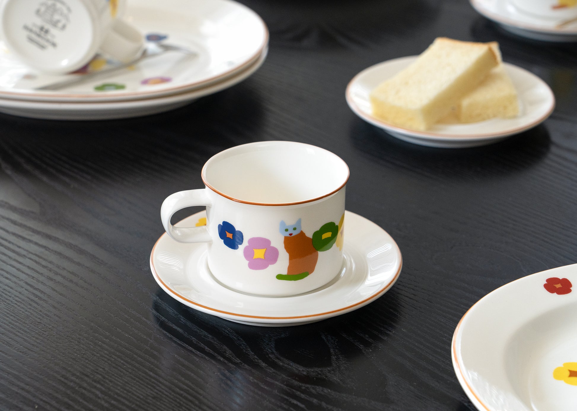 Ceramic cup and saucer with colorful designs on a black table.