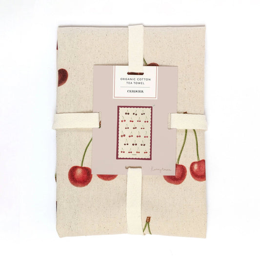 A folded organic cotton tea towel with a cherry print, wrapped in a light beige paper sleeve with elastic bands, on a white background.