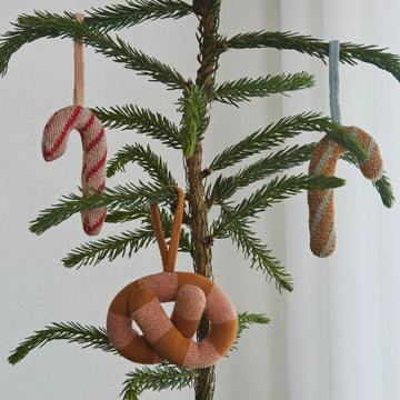 Decorative Christmas ornaments shaped like a pretzel, candy cane, and spiral on a Christmas tree branch.