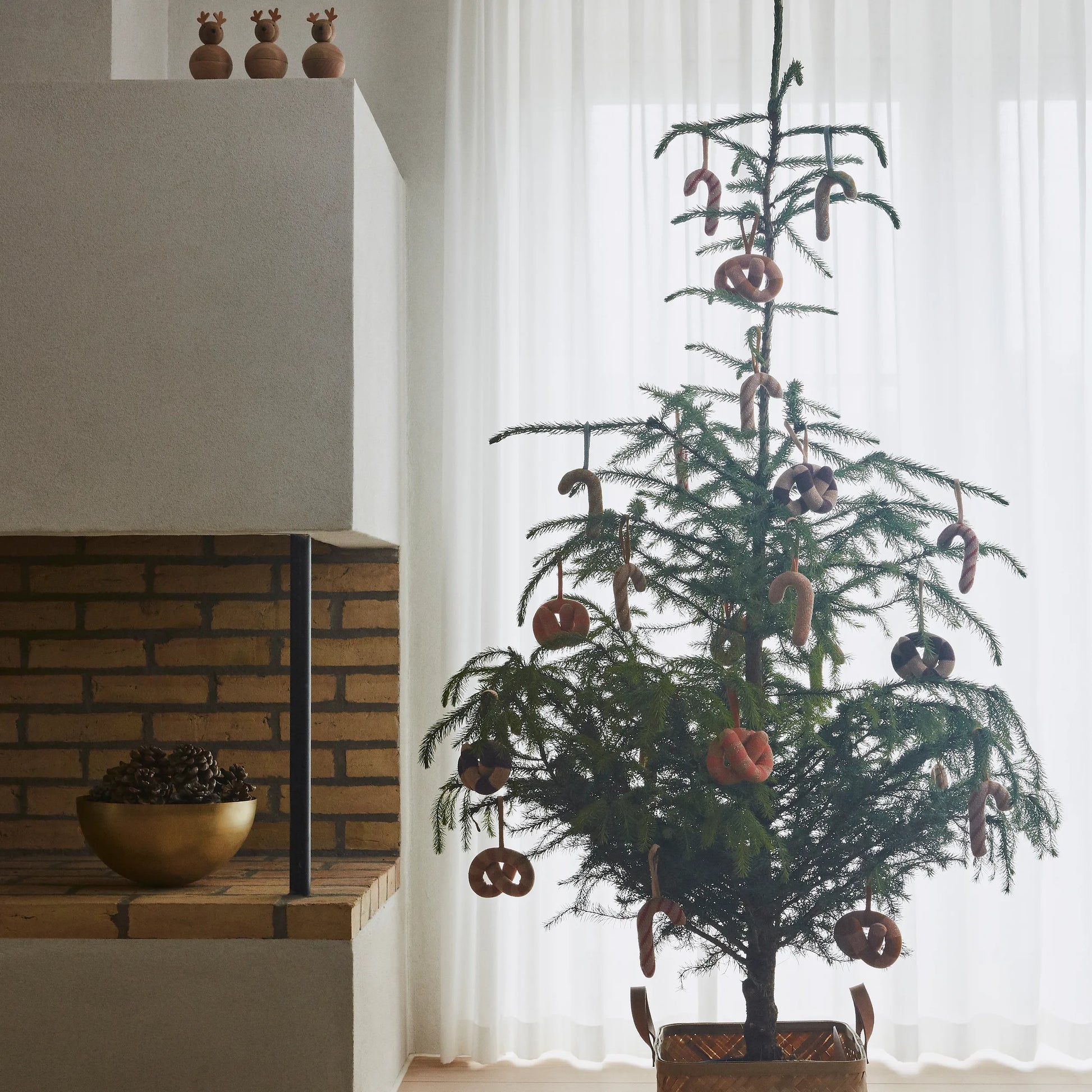 Small decorated Christmas tree in a room with a brick wall and white curtains.