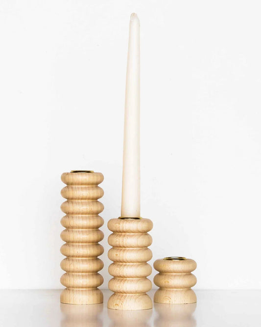 Set of three wooden candle holders with a white candle on a white background