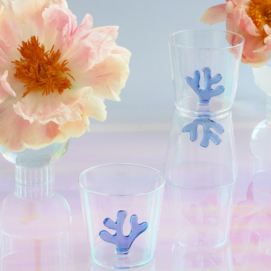 Clear glass carafe and cups with blue coral design inside, surrounded by flowers on a light background