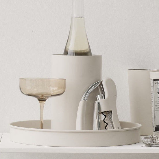 White shelf with decorative items including a bottle, glasses, and books against a light gray wall.