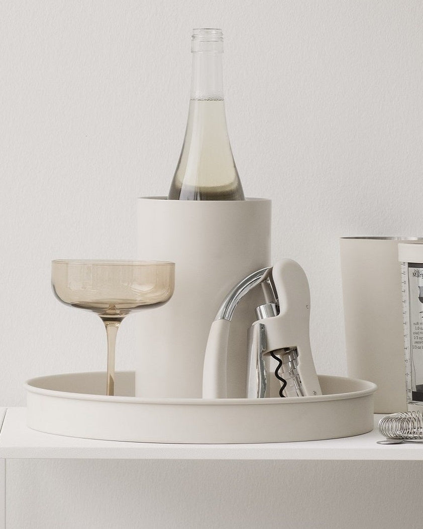 White shelf with decorative items including a bottle, glasses, and books against a light gray wall.