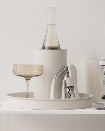 White shelf with decorative items including a bottle, glasses, and books against a light gray wall.