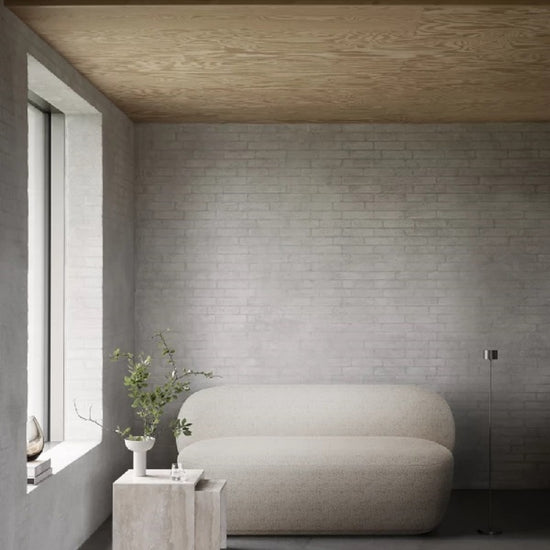 Modern interior with a curved beige sofa against a gray brick wall.