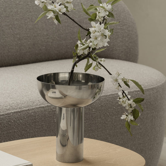 Metallic vase with white flowers on a wooden table in a living room setting.