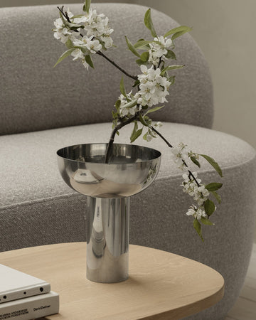 Metallic vase with white flowers on a wooden table in a living room setting.