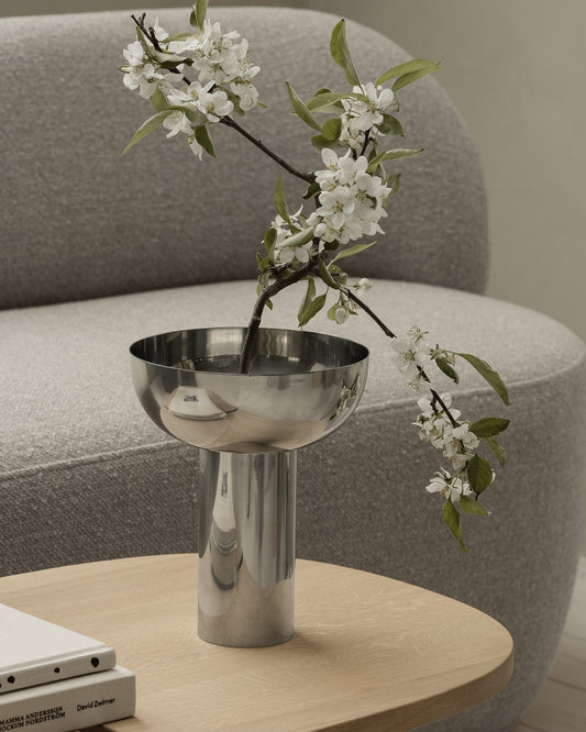 Metallic vase with white flowers on a wooden table in a living room setting.