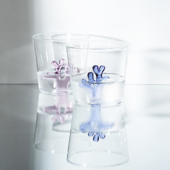 Two clear glass tumblers with pink and blue coral design inside on a reflective surface.