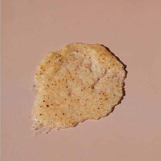 A dollop of textured, speckled beige cosmetic cream or scrub on a solid warm beige background.