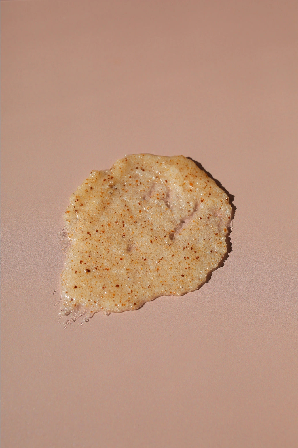 A dollop of textured, speckled beige cosmetic cream or scrub on a solid warm beige background.