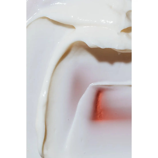 A close-up of a thick, creamy off-white cosmetic or skincare product with smooth, glossy texture and soft shadows.