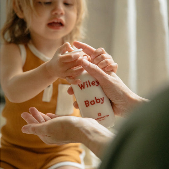 Child holding a bottle labeled 'Wiley Baby' with an adult's hand.