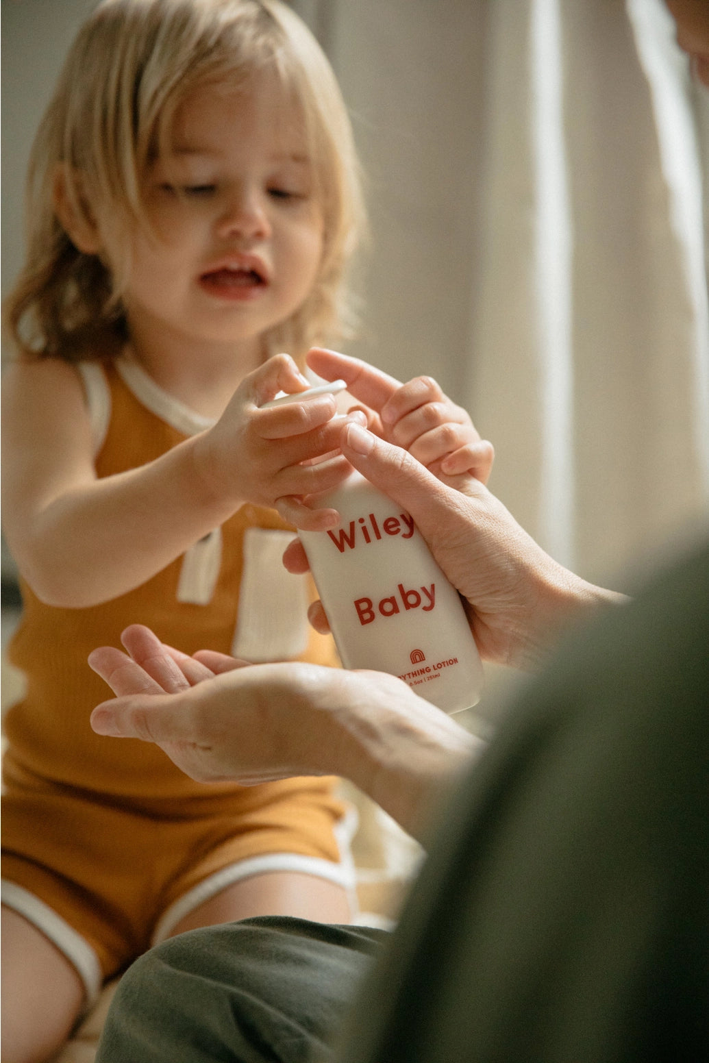 Child holding a bottle labeled 'Wiley Baby' with an adult's hand.