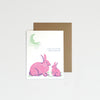 Greeting card with pink bunnies and moon on a light gray background