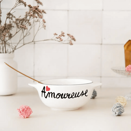 White bowl with 'Amoureuse' text on a white surface with decorative elements.