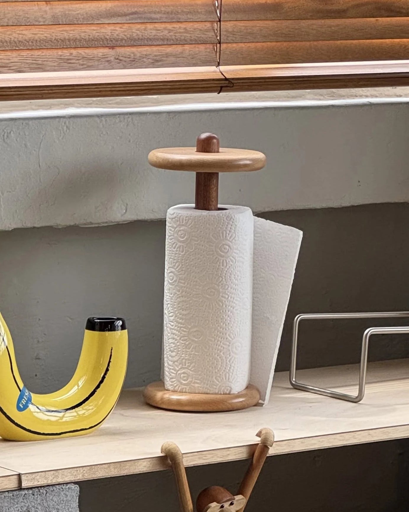 Wooden banana-shaped bottle opener and paper towel holder on a shelf with a monkey figurine.