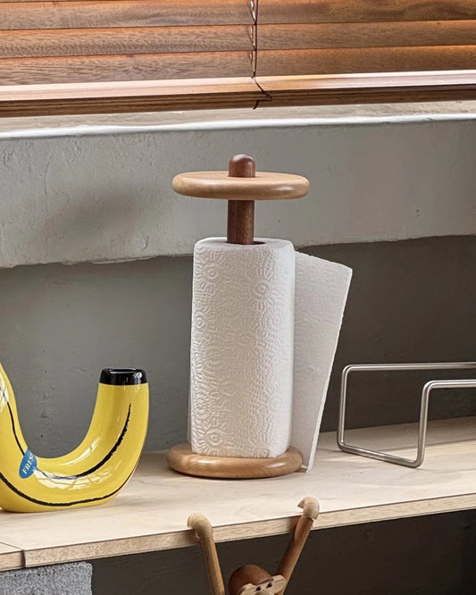 Wooden banana-shaped bottle opener and paper towel holder on a shelf with a monkey figurine.