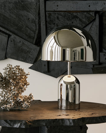 Silver table lamp on a wooden surface with a dark, textured wall in the background