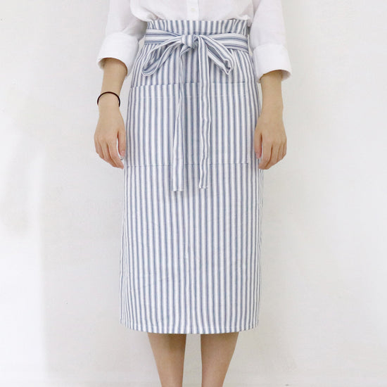 Person wearing a white shirt and striped apron against a plain background